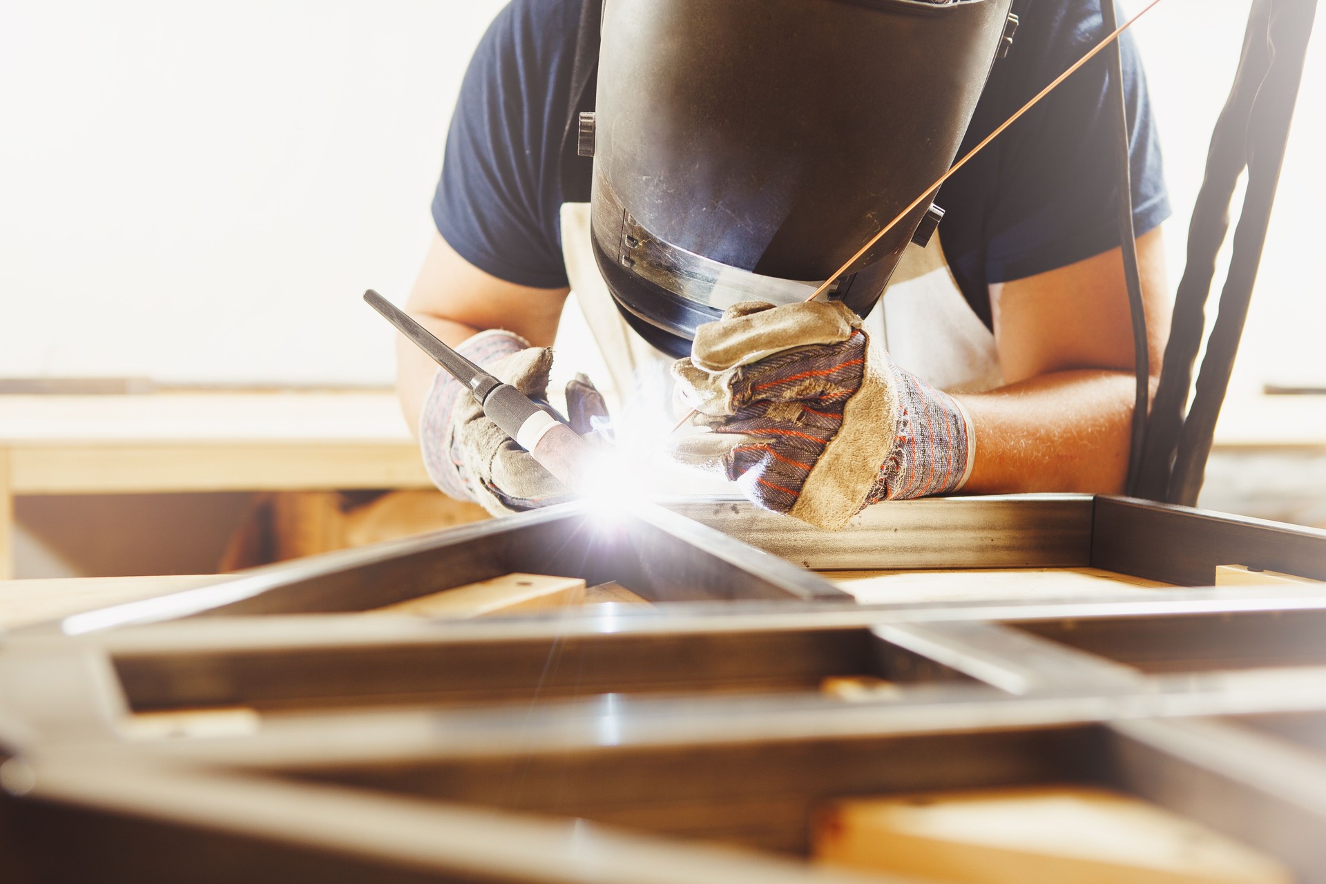 Male in face mask welds with argon-arc welding