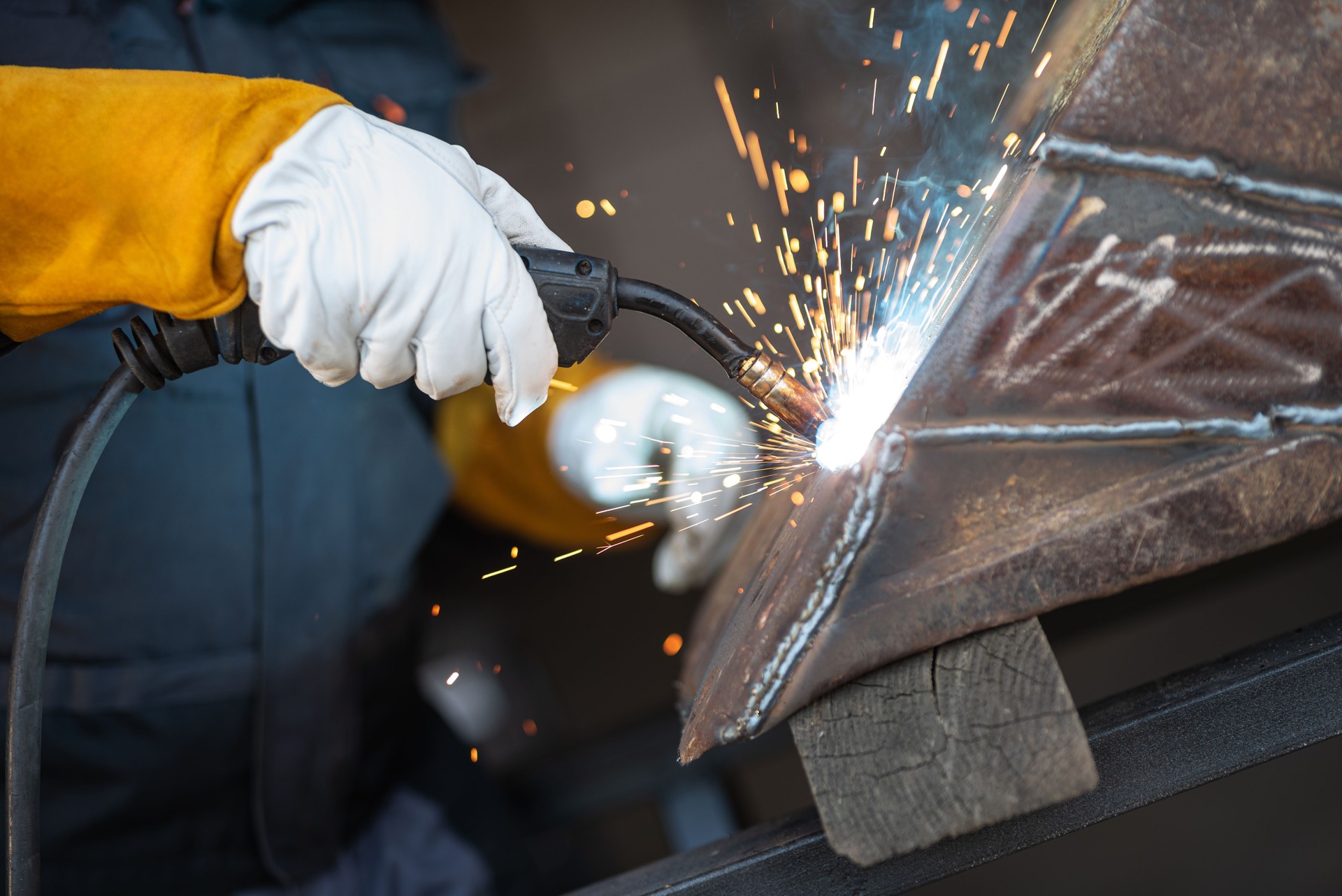 Welder joining metal parts with welding torch creating sparks